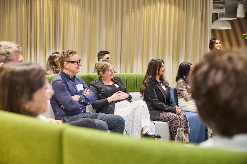 Participants seated on green lounges smile and listen during a Brand Camp session.